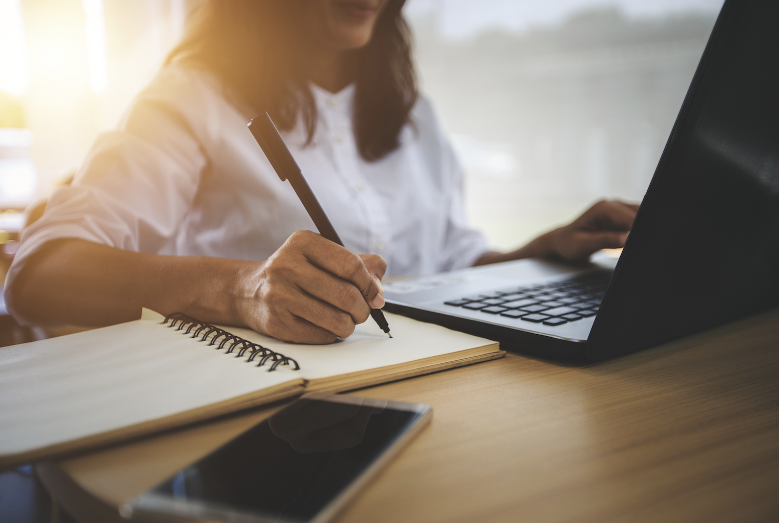 Woman writing at a desk with a computer