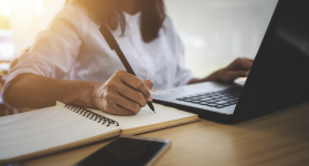 Woman writing at a desk with a computer